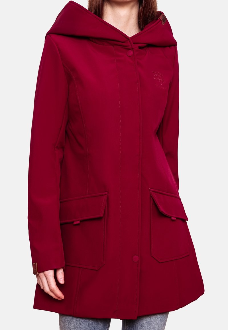 Femme portant un long manteau rouge à capuche avec de grandes poches plaquées à l'avant, une fermeture par boutons et un logo brodé discret sur la poitrine.