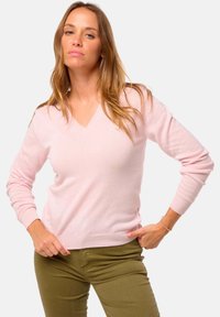 Pull à col en V, à manches longues, en tissu rose doux, avec des poignets et un ourlet côtelés. Associé à un pantalon ajusté vert olive.