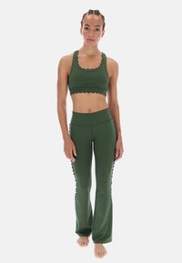 Zielony zestaw sportowy składający się z cropped topu z falbaniastymi brzegami oraz spodni dzwonowych z wysokim stanem i falbaniastymi akcentami po bokach.
