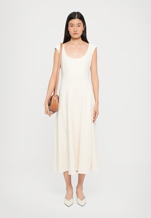 Un vestito midi senza maniche di colore crema con scollo tondo e trama liscia. Abbinato a una borsa a tracolla marrone e scarpe a punta di colore crema.
