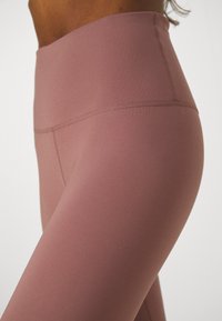 Högmidjade leggings i en dämpad rosafärg, tillverkade av stretchigt tyg med en slät yta och subtila sömdetaljer längs midjebandet.