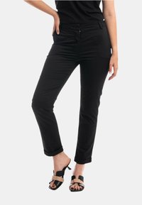 Pantaloni neri con vestibilità slim, dotati di tasche anteriori, zip laterale e risvolti. Abbinati a sandali aperti neri e beige.