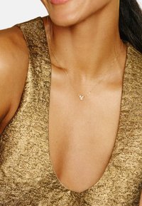 Kultakaulakoru, jossa on pieniä pyöreitä koristeita, puettuna teksturoidun kultakankaisen topin kanssa, jossa on syvä V-kaula-aukko.