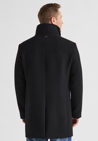 Schwarzer Wollmantel mit hohem Kragen, strukturierter Silhouette und glatter Textur, ausgestattet mit einem Rückentab-Label und geradem Saum.