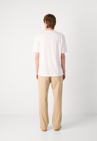 Hvit bomull t-skjorte med korte ermer og rund hals, kombinert med beige, løstsittende bukser. Enkel, moderne design.