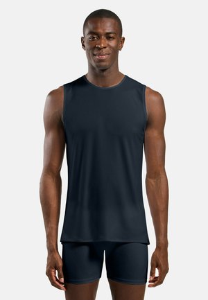 Mann steht, trägt ein schwarzes ärmelloses Sportoberteil und passende schwarze Shorts vor einem schlichten hellen Hintergrund.