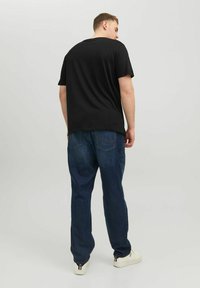 Schwarzes Baumwoll-T-Shirt mit kurzen Ärmeln und Rundhalsausschnitt, kombiniert mit locker sitzenden blauen Jeans und weißen Sneakers.