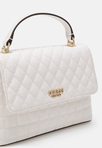 Prošívaná bílá kabelka se zlatými kovovými prvky, vybavená horním držadlem a vyraženým logem. Texturovaný povrch s hladkou podšívkou.