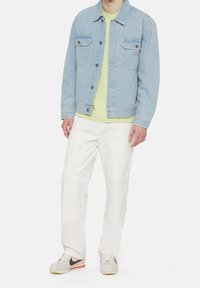 Ljusblå denimjacka med två bröstfickor, matchad med en limegrön T-shirt, vita byxor och ljusgrå sneakers med röda detaljer.