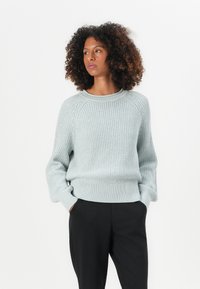 Svijetloplavi pleteni pulover s rebrastom teksturom, okruglim izrezom i spuštenim ramenima, uparen s crnim hlačama.