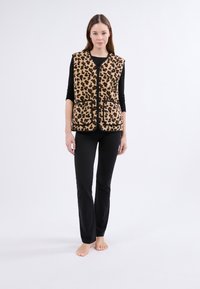 Kamizelka w panterkę o miękkiej teksturze, z zamkiem z przodu i dwiema dużymi kieszeniami, zestawiona z czarnymi dopasowanymi spodniami.