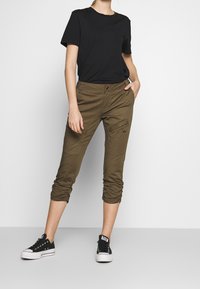 Černé tričko s krátkým rukávem zkombinované s olivově zelenými zkrácenými cargo kalhotami s boční kapsou a staženými manžetami, doplněné černými teniskami.