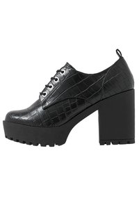 Zapatos de tacón negros con textura de cocodrilo brillante, punta redonda, diseño de cordones y suela de plataforma gruesa con detalles acanalados.