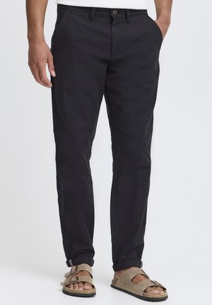 Black cotton chinos with a slim fit, featuring a button closure, side pockets, and a smooth texture, paired with brown sandals.
