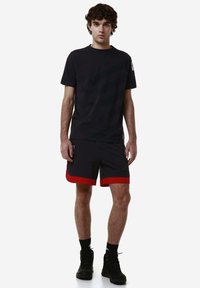 T-shirt nera a maniche corte con strisce orizzontali, abbinata a pantaloni corti grigi con accenti rossi. Il modello indossa calzini neri e stivali.