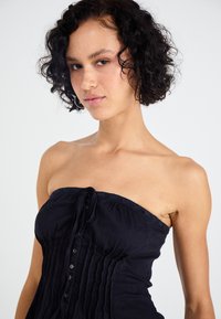 Μαύρο strapless τοπ με κλείσιμο με κουμπί και πτυχωτό σχέδιο. Διαθέτει δαντελένια λεπτομέρεια στη λαιμόκοψη και απαλό υφασμάτινο πέρισμα.