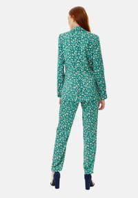 Green patterned suit featuring a jacket with a collar and matching slim-fit trousers. Fabric has a textured, vibrant design with accents.