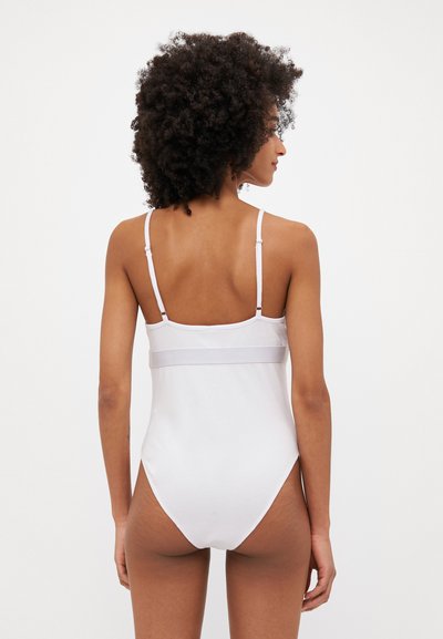 Costume da bagno intero bianco con spalline regolabili, una texture liscia e un design a gamba alta, con un semplice dettaglio sul retro.