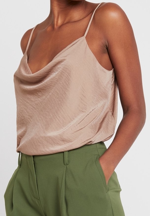 Camisole beige soyeuse avec un décolleté drapé, des bretelles fines et une coupe décontractée, associée à un pantalon vert taille haute.