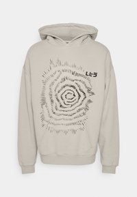 Sweat à capuche beige avec un motif graphique en spirale noir. Comprend une poche avant et une capuche avec cordon de serrage. Tissu doux, coupe décontractée.