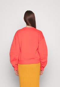 Maglione color corallo con spalle scese e orlo a coste, abbinato a una gonna gialla a coste. Texture liscia con pochi dettagli hardware.