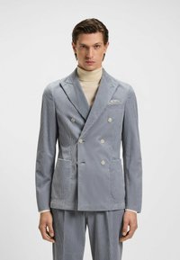 Giacca da abito grigia in corduroy doppiopetto con revers a punta, due tasche frontali e un fazzoletto decorativo. Tessuto morbido e vestibilità su misura.