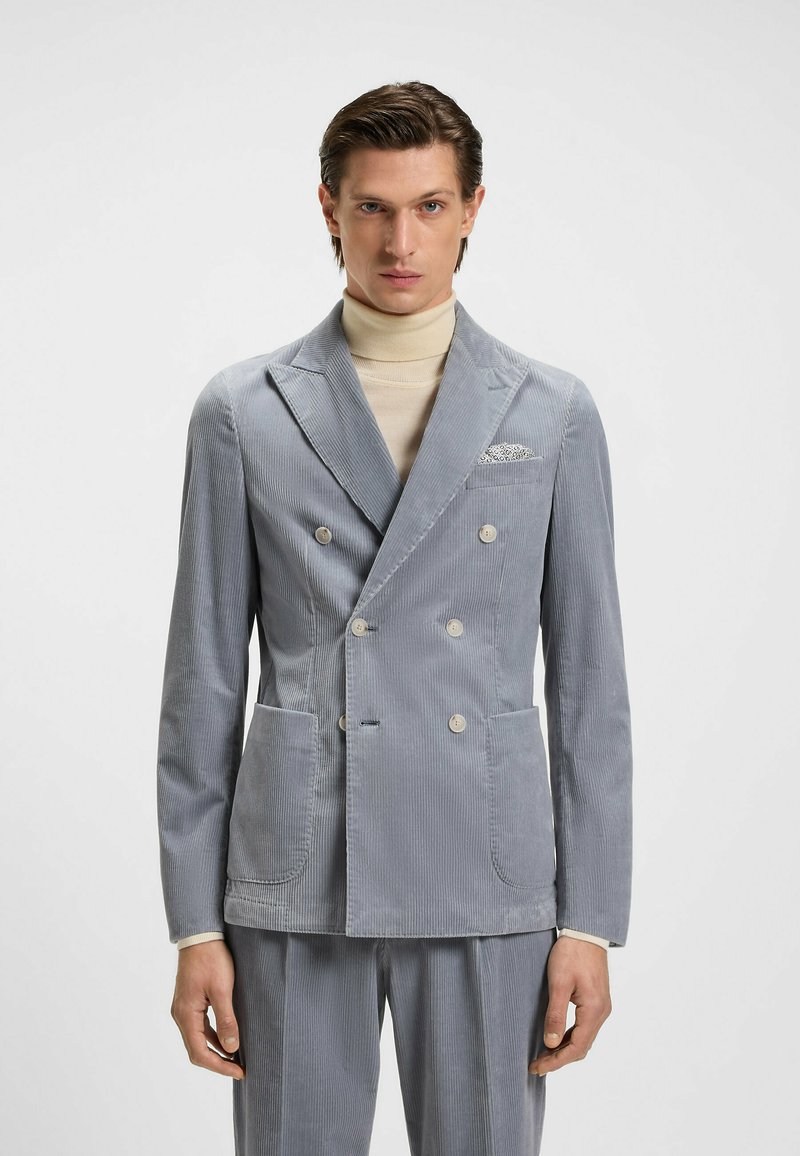 Giacca da abito grigia in corduroy doppiopetto con revers a punta, due tasche frontali e un fazzoletto decorativo. Tessuto morbido e vestibilità su misura.