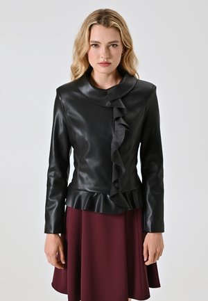 Giacca in pelle nera con dettaglio arricciato sul davanti, colletto alto e orlo peplum. Indossata sopra una gonna bordeaux, con maniche lunghe.