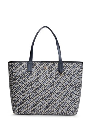 Beige tote-taske med navyblåt sammenflettet geometrisk mønster, navyblå håndtag og lille gylden logoemblem på fronten.