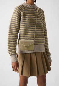 Maglione a righe beige e oliva con scollatura e polsini a costine, abbinato a una gonna plissettata kaki e una borsa a tracolla metallica dorata.