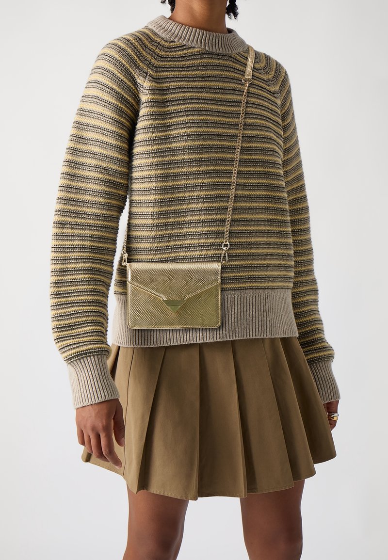 Maglione a righe beige e oliva con scollatura e polsini a costine, abbinato a una gonna plissettata kaki e una borsa a tracolla metallica dorata.