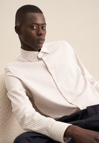 Camicia button-up a righe rosa chiaro e bianco con colletto, realizzata in tessuto morbido, presenta una vestibilità rilassata e bottoni a vista.