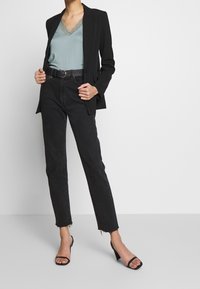 Black blazer over a teal camisole with lace trim, paired with high-waisted black jeans featuring frayed hems and black strappy heels.