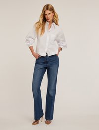 Witte, gekraagde, button-up overhemd met een enkele borstzak, gecombineerd met blauwe, rechtvallende spijkerbroeken en bruine hoge hakken sandalen.