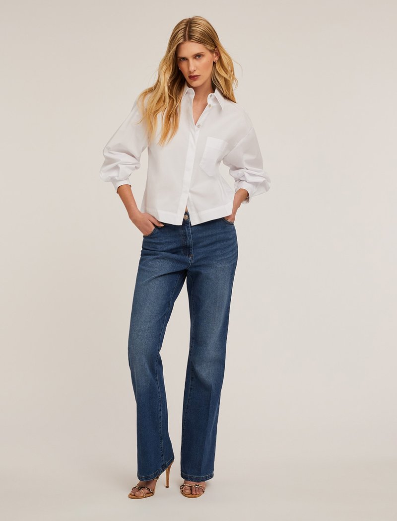 Witte, gekraagde, button-up overhemd met een enkele borstzak, gecombineerd met blauwe, rechtvallende spijkerbroeken en bruine hoge hakken sandalen.