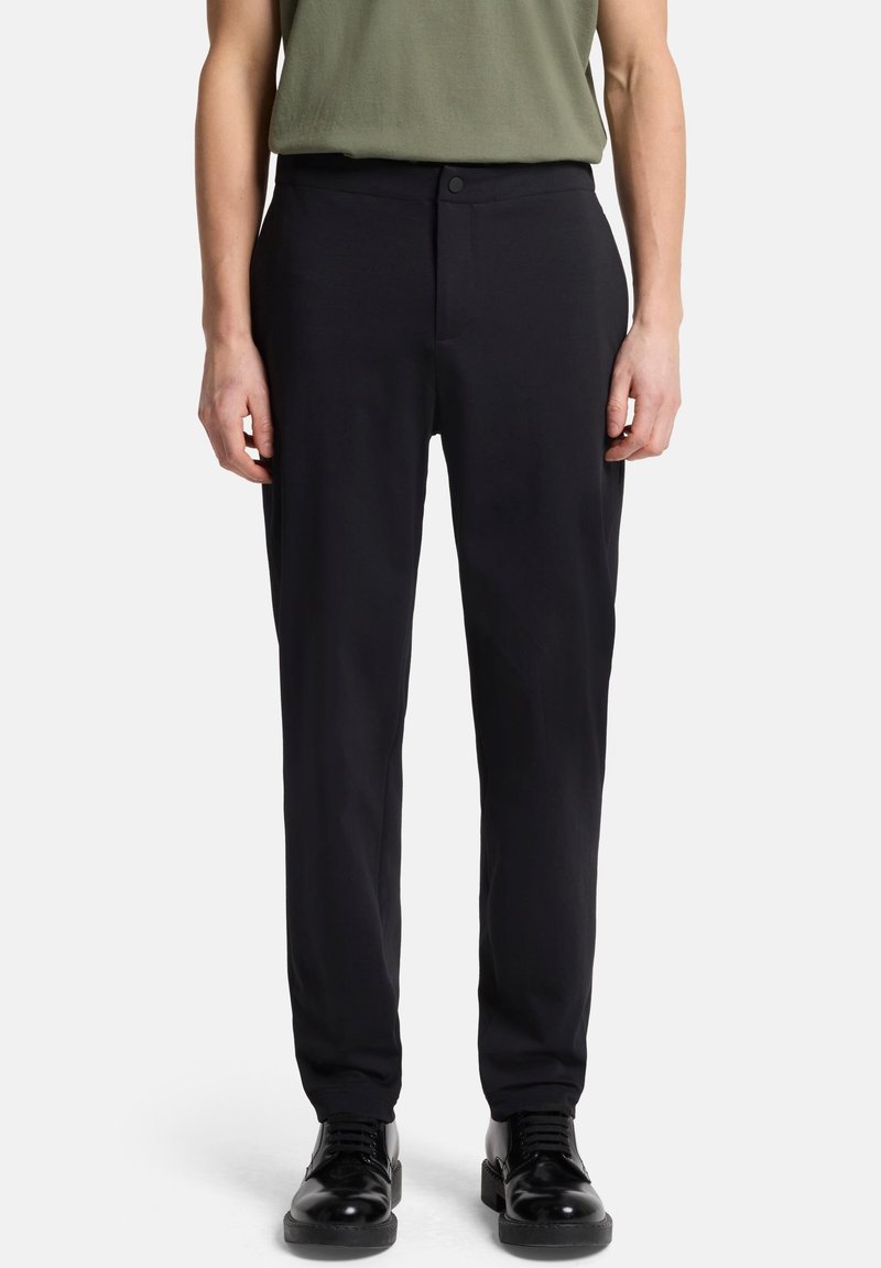 Schwarze, maßgeschneiderte Hose mit geradem Schnitt aus glattem Stoff. Mit Knopfverschluss und Seitentaschen. Kombiniert mit einem grünen Oberteil.