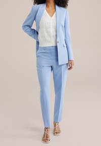 Ljusblå skräddarsydd kostym med enbladsblazer och slim fit-byxor, kombinerad med en vit stickad topp. Utrustad med stiliga sandaler.