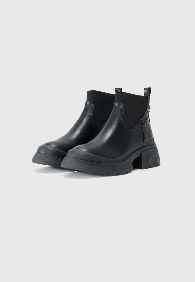 Bottines en cuir noir avec une semelle en caoutchouc épaisse, des panneaux latéraux élastiques et des tirettes pour un enfilage facile. Texture lisse et design épuré.