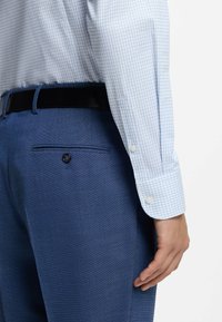Camicia a quadri azzurro chiaro e bianca con polsini con bottoni abbinata a pantaloni blu scuro con trama, caratterizzati da una tasca posteriore e dettaglio con bottone.