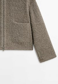 Ruskea teksturoitu takki, jossa vetoketjullinen suljenta ja yksi tasku; valmistettu pehmeästä, kudotusta materiaalista, jolla on hieman pörröinen pinta.