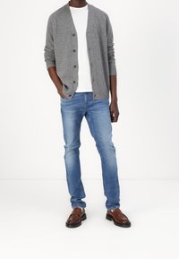 Cárdigan gris de punto con botones sobre una camiseta blanca, combinado con jeans de tela azul claro y mocasines de cuero marrón. Diseño sencillo y casual.