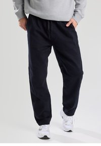 Navy blue cotton jogger pants with an elastic waistband and cuffs, featuring side pockets and a drawstring detail at the waist.