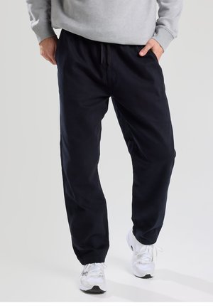 Navy blue cotton jogger pants with an elastic waistband and cuffs, featuring side pockets and a drawstring detail at the waist.