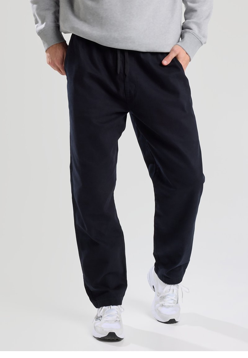 Navy blue cotton jogger pants with an elastic waistband and cuffs, featuring side pockets and a drawstring detail at the waist.