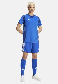 Blaues Sporttrikot und Shorts mit dunkelblauen Akzenten, weißen Streifen und Logo. Lange blaue Socken und weiße Stollenschuhe vervollständigen das Outfit.