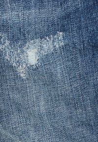 Blå denimtyg med ett litet slitet och fransigt område som visar vita trådar ochslitet mönster.