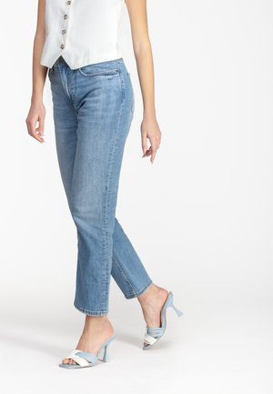 Jeans aderenti azzurri con vita media, caratterizzati da un classico design a cinque tasche. Abbinati a sandali con tacco blu e bianchi.