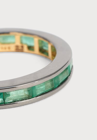 Bague en argent avec des pierres précieuses rectangulaires vertes disposées en ligne continue autour de l'anneau, présentée sur un fond clair uni.