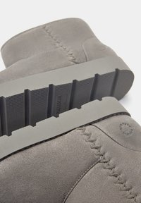 Bottines en suede gris avec une semelle en caoutchouc striée, des détails de couture et un logo circulaire sur le côté. Texture lisse sur l'ensemble.