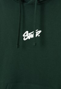 Sweat à capuche vert foncé avec un logo stylisé "Smp." blanc centré sur la poitrine et des cordons verts assortis suspendus à la capuche.
